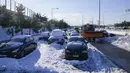 Sebuah bajak salju melewati kendaraan terbengkalai yang terjebak dalam salju di jalan raya Attiki Odos, menyusul hujan salju lebat pada Selasa di Athena, Rabu (26/1/2022). Pihak berwenang berupaya membersihkan jalan yang terblokir dan memulihkan aliran listrik yang padam. (AP/Thanassis Stavrakis)