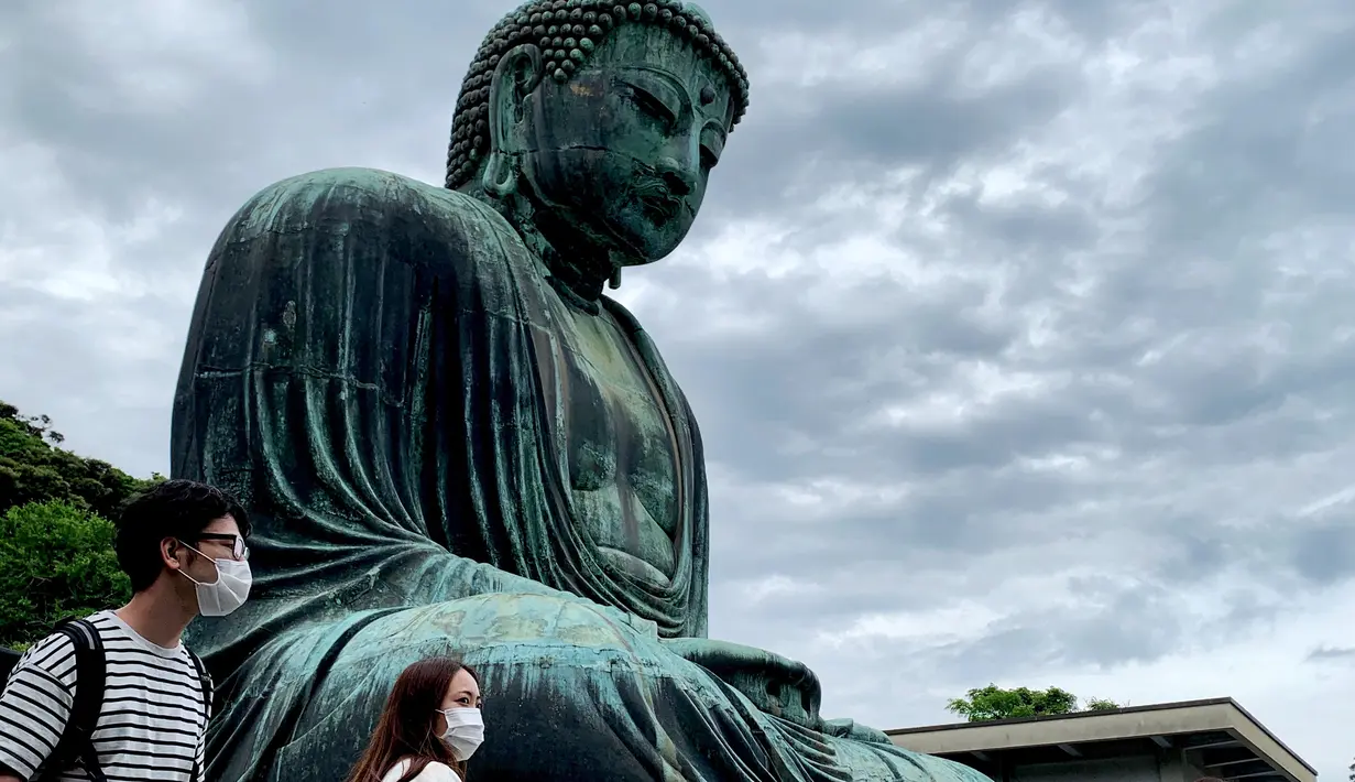 Orang-orang mengenakan masker saat mengunjungi The Great Buddha atau yang biasa disebut Kamakura Daibutsu di kuil Kotoku-in di Kamakura, Prefektur Kanagawa, Jepang, Sabtu (20/6/2020). Patung Buddha dari perunggu yang menjulang dengan tinggi 13,35 meter ini didirikan tahun 1252. (Behrouz MEHRI/AFP)