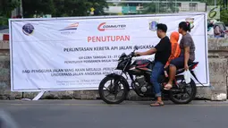 Warga membaca spanduk sosialisasi penutupan perlintasan kereta di Jalan Angkasa, Jakarta, Minggu (15/10). Penutupan secara permanen perlintasan KA di Jalan Angkasa akan dilakukan pada 3 November mendatang. (Liputan6.com/Helmi Fithriansyah)