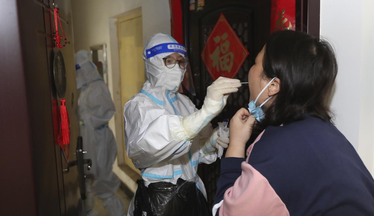 Seorang pekerja medis mengambil sampel swab dari seorang warga selama pemeriksaan Covid-19 dari pintu ke pintu di Kota Zhengzhou, China Tengah, Selasa (1/11/2022). Para pekerja iPhone Apple Inc meninggalkan pabrik karena lokasinya berada dalam zona industri Kota Zhengzhou yang sedang diberlakukan lockdown setelah adanya 64 laporan kasus virus corona di kawasan tersebut. (Chinatopix via AP)