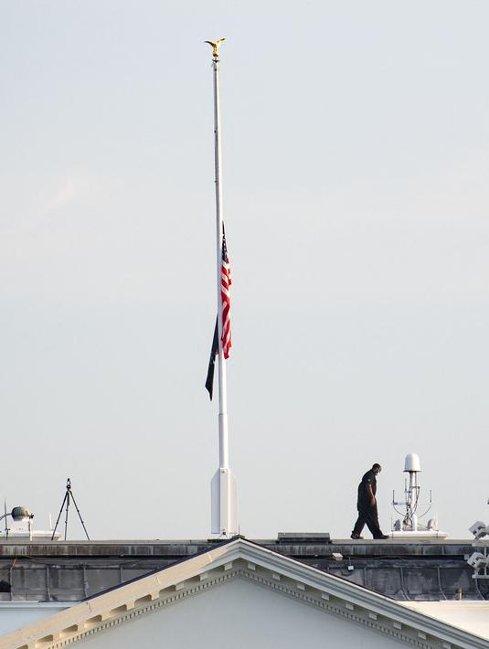 Petugas Secret Service berjalan kembali setelah menurunkan bendera AS yang berkibar setengah tiang di atas Gedung Putih, Kamis (26/8/2021). Pengibaran bendera AS setengah tiang itu untuk menghormati anggota marinir AS dan lainnya yang tewas dalam serangan bom di Kabul, Afghanistan (Eric BARADAT/AFP)