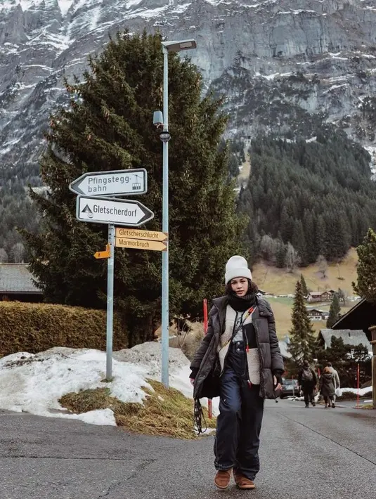 Berlibur di Swiss, Andien Aisyah tampil dengan outfit berlapis. Ia mengenakan coat winter di atas jaket dan sweater. Dipadu celana panjang dan beanie. [Instagram].