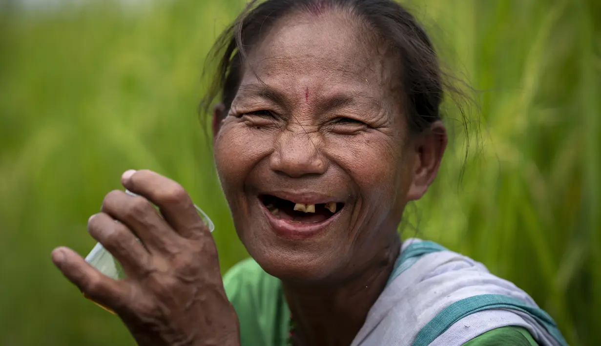 Seorang wanita suku Karbi tersenyum saat dia istirahat minum teh saat memanen padi di sebuah ladang di pinggiran Gauhati, India, Senin (23/5/2022). Suku Karbi adalah salah satu komunitas etnis utama di India Timur Laut yang sebagian besar terkonsentrasi di distrik perbukitan Karbi Anglong di Assam. (AP Photo/Anupam Nath)