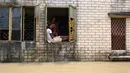 Warga duduk di jendela rumahnya ketika banjir merendam Ghatal, distrik Paschim Medinipur, sekitar 100 km dari Kolkata (2/8/2021). Perahu menjadi andalan warga untuk beraktivitas saat banjir. (AFP/Dibyangshu Sarkar)