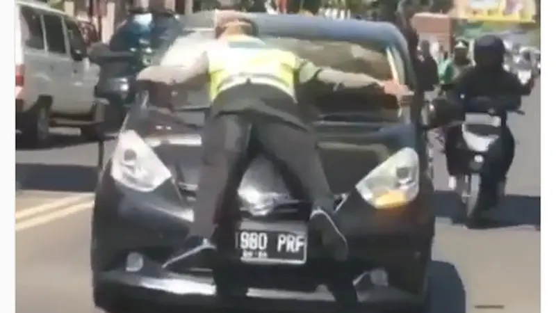 Terlihat jelas polisi tersebut berpegang pada kedua mobil saat kendaraan melaju dengan kecepatan sedang.