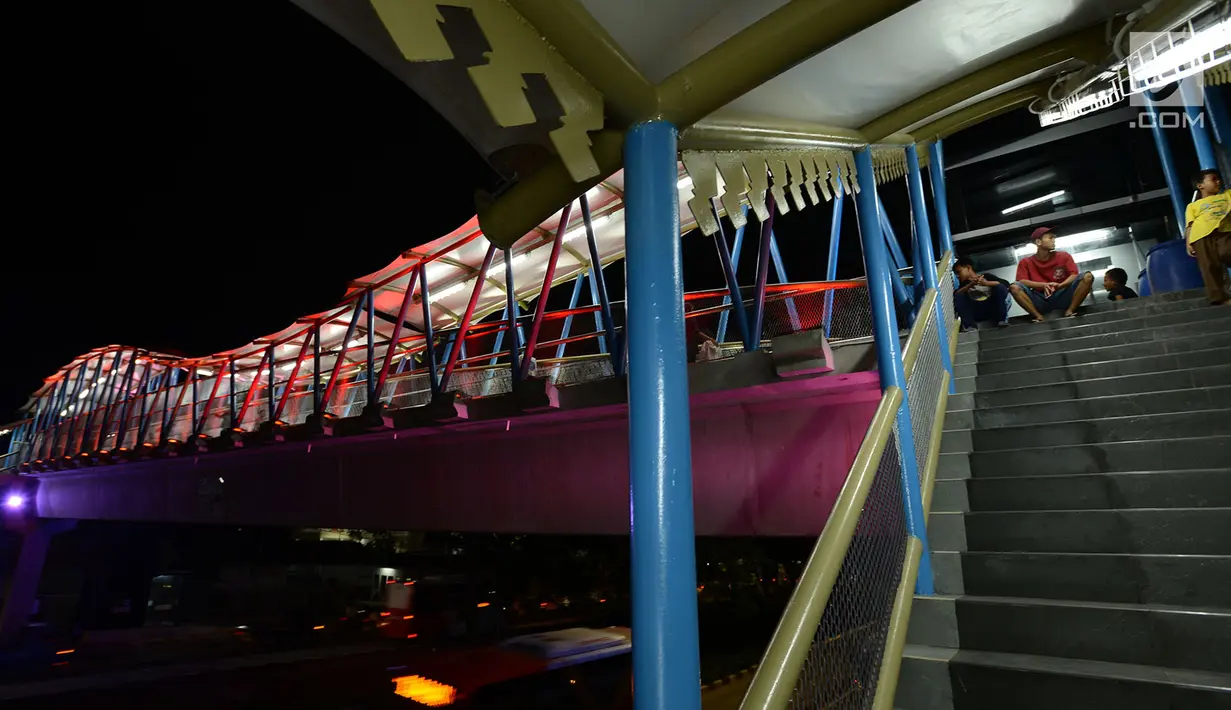 Sejumlah remaja duduk di tangga jembatan penyeberangan orang (JPO) di kawasan Jakarta Timur, Kamis (27/12). JPO ini dihiasi warna warni lampu dengan fasilitas lift untuk para disabilitas menyeberang jalan. (Merdeka.com/Imam Buhori)