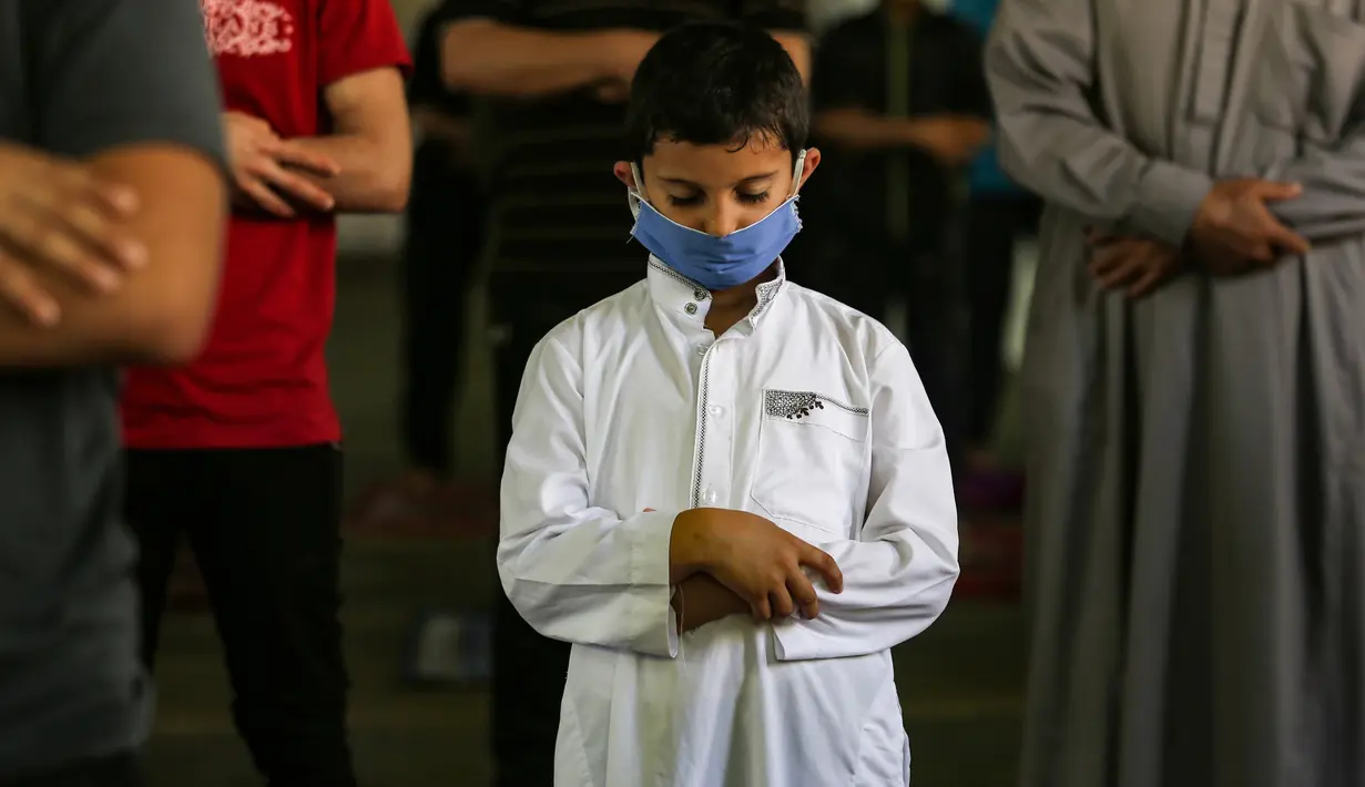 Seorang anak Palestina mengenakan masker saat ambil bagian dalam salat zuhur di masjid Al-Abrar di Rafah, selatan Jalur Gaza, Rabu (3/6/2020). Masjid-masjid kembali dibuka bagi jemaah menyusul pelonggaran pembatasan Covid-19 di Jalur Gaza. (Photo by SAID KHATIB / AFP)