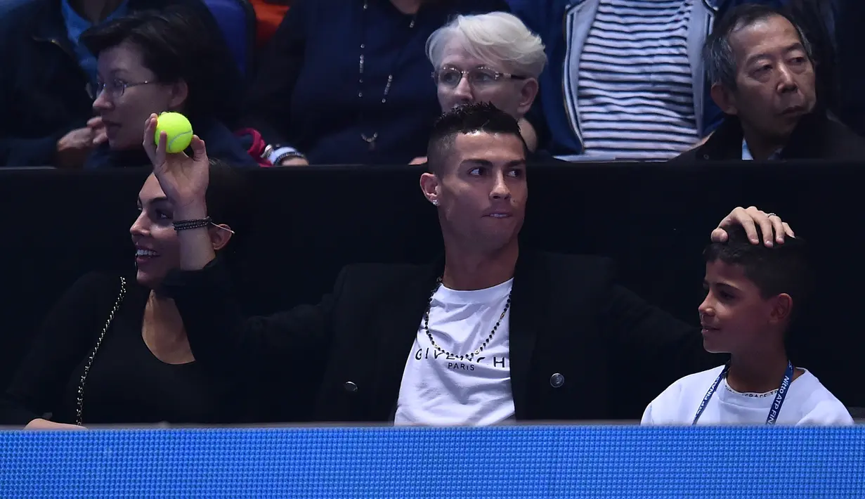 Pemain Juventus, Cristiano Ronaldo menangkap bola tenis yang mengarah kepadanya dan sang kekasih, Georgina saat menyaksikan Novak Djokovic menghadapi John Isner pada laga tenis dunia, ATP Finals 2018, di O2 Arena, London, Senin (12/11). (Glyn KIRK/AFP)