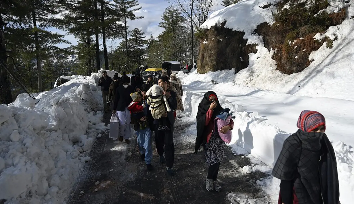 Wisatwan berjalan di sepanjang jalan Bukit Murree yang tertutup salju, Pakistan, 9 Januari 2022. Sebanyak 22 wisatawan tewas saat sekitar 1.000 kendaraan terjebak salju tebal di Bukit Murree. (Aamir QURESHI/AFP)