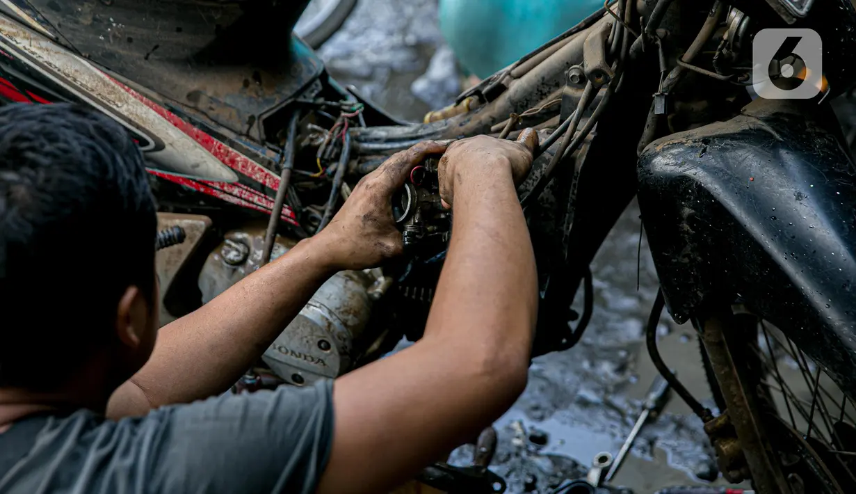 Montir memperbaiki sepeda motor konsumen usai terendam banjir di kawasan Mampang, Jakarta, Minggu (21/2/2021). Banjir yang melanda Ibu Kota Jakarta pada Sabtu (20/2) menyebabkan banyak kendaraan warga mengalami kerusakan akibat terendam air. (Liputan6.com/Faizal Fanani)