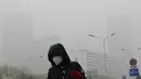 Seorang wanita beraktivitas mengenakan masker di sebuah jalan yang diselimuti kabut asap tebal di Beijing, China (14/11). Pihak berwenang mengeluarkan peringatan kuning untuk polusi udara buruk pada hari Rabu. (AP Photo/Andy Wong)