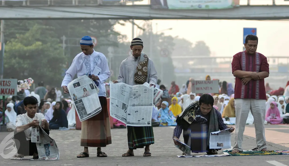 Warga menggelar koran sebagai alas untuk melaksanakan salat Idul Fitri di kawasan Jatinegara, Jakarta, Rabu (6/7). Ruas Jalan Jatinegara Barat disulap menjadi tempat pelaksanaan salat . (Liputan6.com/Yoppy Renato)