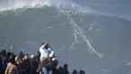 Orang-orang menyaksikan peselancar menaiki ombak saat sesi selancar ombak besar di Praia do Norte atau Pantai Utara, di Nazare, Portugal, (8/1/2022). Setiap tahunnya peselancar profesional menantang adrenalinnya mengarungi ombak besar dan tinggi di Pantai Praia do Norte. (AP Photo/Armando Franca)
