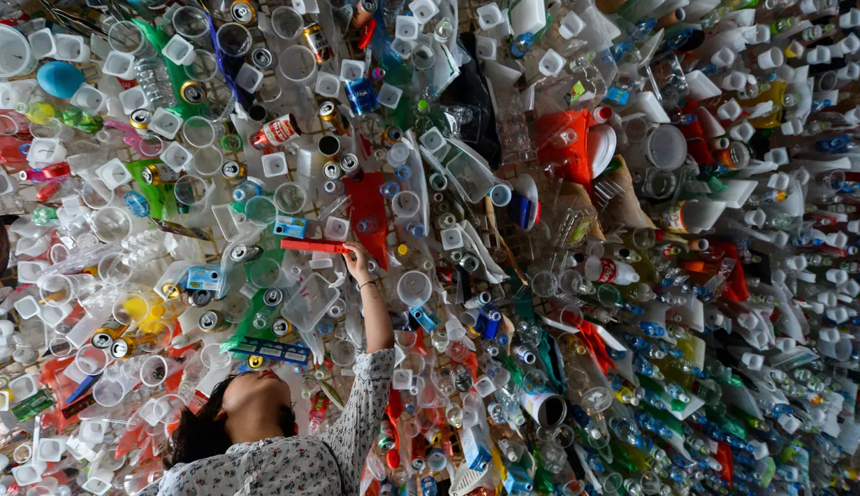 Seorang wanita melihat instalasi seni gantung sekelompok seniman yang terbuat dari sisa-sisa plastik, kaleng dan wadah di sebuah pameran "Reduce the Litter" di Pusat Kebudayaan Prancis di Hanoi (15/7/2019). Pameran ini mengambil perspektif tentang produksi dan konsumsi. (AFP Photo/Nhac Nguyen)