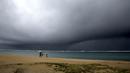 Orang-orang memegang payung saat hujan mulai turun di pantai yang kosong di Honolulu  (6/12/2021). Pihak berwenang mengatakan kondisi yang berpotensi lebih buruk ke depannya. (AP Photo/Caleb Jones)