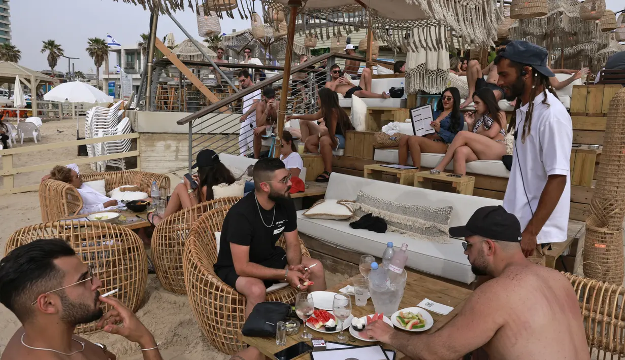 Orang-orang bersantai di bar pantai di kota pesisir Israel Tel Aviv (19/4/2021). Pemerintah Israel mencabut kewajiban memakai masker setelah 81 persen penduduk dewasa menerima vaksin Covid-19. (AFP/menahem kahana)
