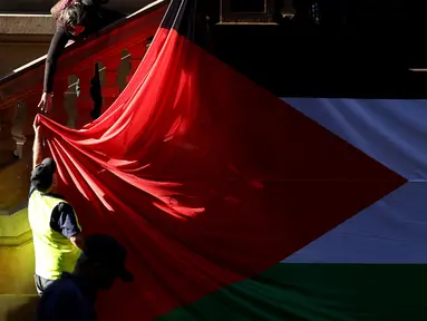 Para pengunjuk rasa menggantungkan bendera Palestina berukuran besar di dinding Balai Kota pada awal unjuk rasa menentang aksi militer Israel di Gaza saat mereka berkumpul di Sydney pada 9 Oktober 2023. (David GRAY/AFP)