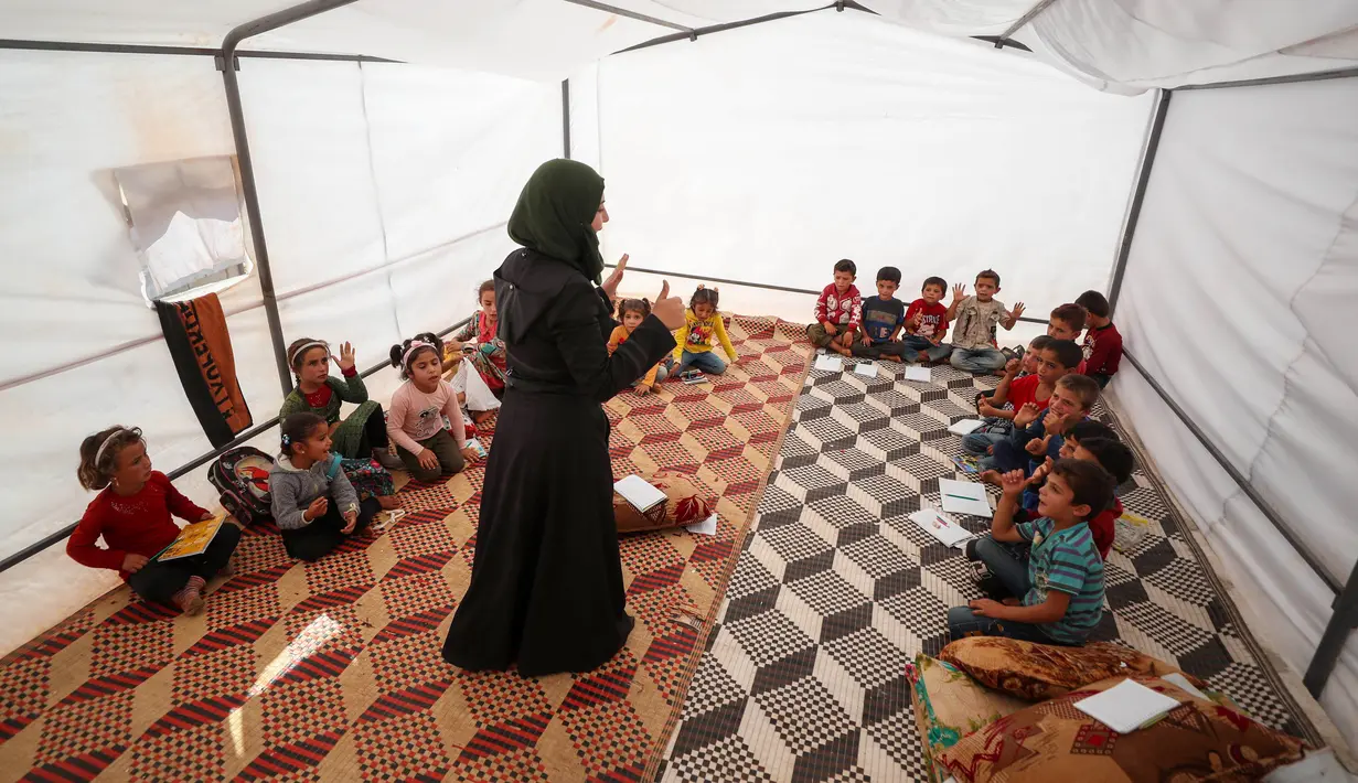 Seorang guru menerangkan pelajaran kepada anak-anak Suriah yang terlantar di dalam tenda yang diubah menjadi ruang kelas di kamp pengungsi di kota Maarrat Misrin di Provinsi Idlib, Suriah (6/10/2020). (AFP/Omar Haj Kadour)