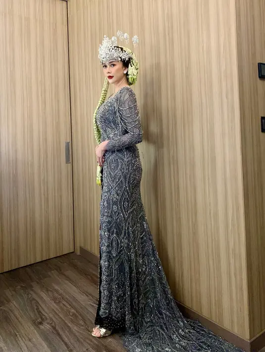 Aura Kasih memadukan penampilannya dengan gaun malam bernuansa biru keabu-abuan penuh batu dan payet, berlengan panjang, dengan siger pengantin dan ronce bunga melatinya. [Foto: Instagram/aurakasih]