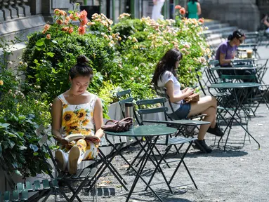 Orang-orang duduk di bawah sinar matahari pada hari yang hangat di Bryant Park di New York City (7/6/2021). Cuaca yang hangat di New York dimanfaatkan warga untuk membaca buku hingga berjalan-jalan. (AFP/Angela Weiss)