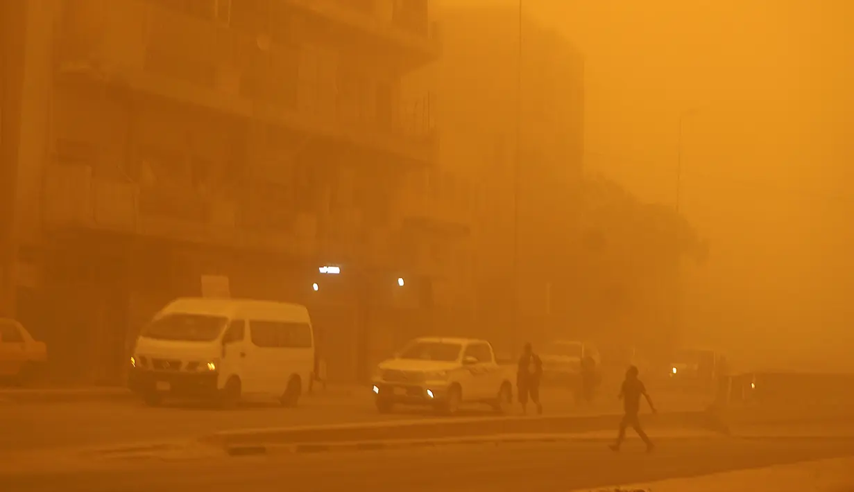 Pejalan kaki menyeberang jalan saat kendaraan melaju di tengah badai debu berat di Baghdad, Irak, Senin (16/5/2022). (Sabah ARAR/AFP)