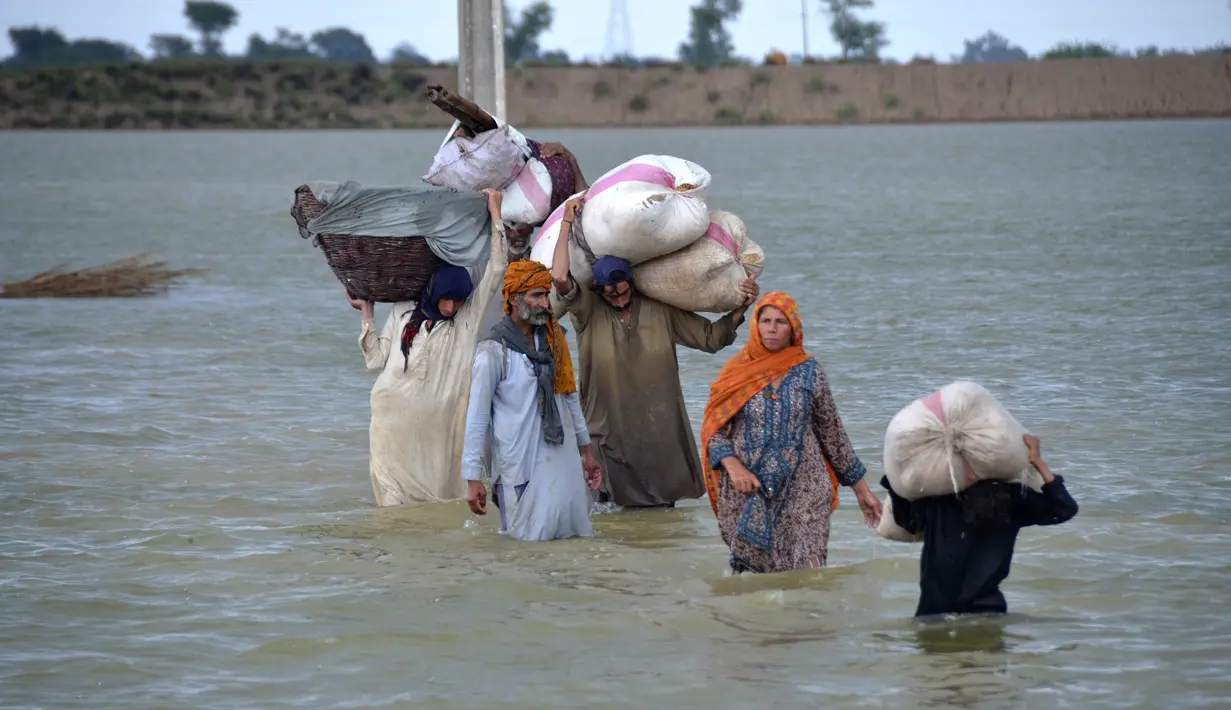 Sebuah keluarga pengungsi mengarungi daerah banjir setelah hujan deras, di Jaffarabad, sebuah distrik di provinsi Baluchistan barat daya Pakistan, Rabu (24/8/2022). Hujan deras telah memicu banjir bandang dan mendatangkan malapetaka di banyak tempat. (AP Photo/Zahid Hussain)