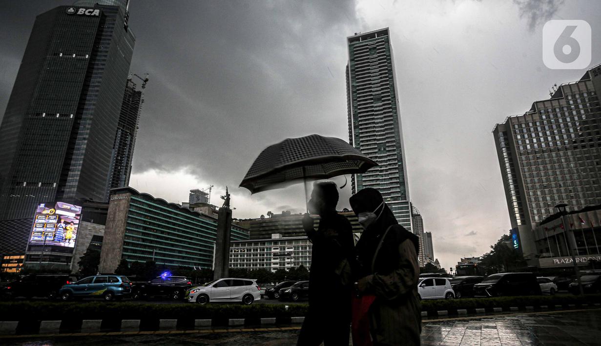 Warga menggunakan payung melintas di kawasan Bundaran Hi, Jakarta, Sabtu (13/11/2021). Badan Meteorologi Klimatologi dan Geofisika (BMKG) melansir peringatan terbaru yang berlaku 7-9 November 2021 soal peringatan cuaca ekstrem imbas dari La Nina. (Liputan6.com/Faizal Fanani)