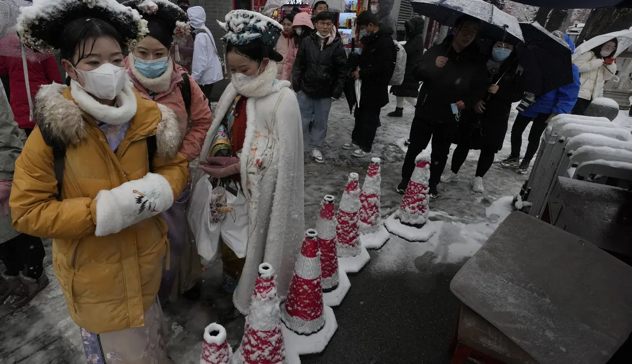 Pengunjung mengenakan kostum periode tradisional berangkat dari Kota Terlarang saat salju turun di Beijing, China (18/3/2022). Gelombang dingin melanda banyak bagian China, menyebabkan suhu turun dan mengganggu lalu lintas di daerah yang terkena dampak. (AP Photo/Ng Han Guan)