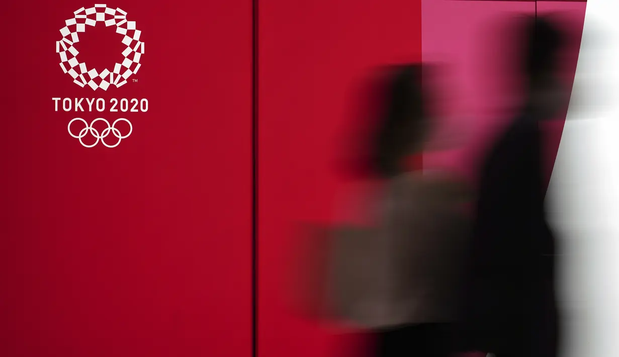 Orang-orang yang memakai masker untuk mencegah penyebaran virus corona berjalan di depan iklan Olimpiade Tokyo 2020 di Tokyo (17/3/2021). Ibukota Jepang mengonfirmasi lebih dari 400 kasus virus korona baru pada hari Rabu. (AP Photo/Eugene Hoshiko)