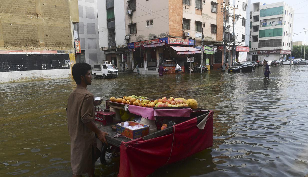 Seorang penjual buah mendorong gerobaknya melintasi jalan yang banjir setelah hujan lebat di Karachi (26/7/2022). Keadaan darurat cuaca diumumkan di Karachi karena hujan muson yang lebih deras dari biasanya terus melanda kota terbesar di Pakistan, membanjiri rumah-rumah dan membuat jalan-jalan tidak dapat dilalui. (AFP/Asif Hassan)