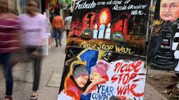 Para pejalan kaki berjalan melewati lukisan untuk memberikan penghormatan kepada para korban perang pada malam peringatan satu tahun invasi Rusia ke Ukraina, di Mumbai, India, Kamis 23 Februari 2023. Invasi Rusia ke Ukraina merupakan salah satu yang terbesar di Eropa sejak Perang Dunia II, ratusan ribu jiwa menjadi korban di kedua pihak, serta menciptakan krisis pengungsi terbesar di Eropa. (Punit PARANJPE/AFP)