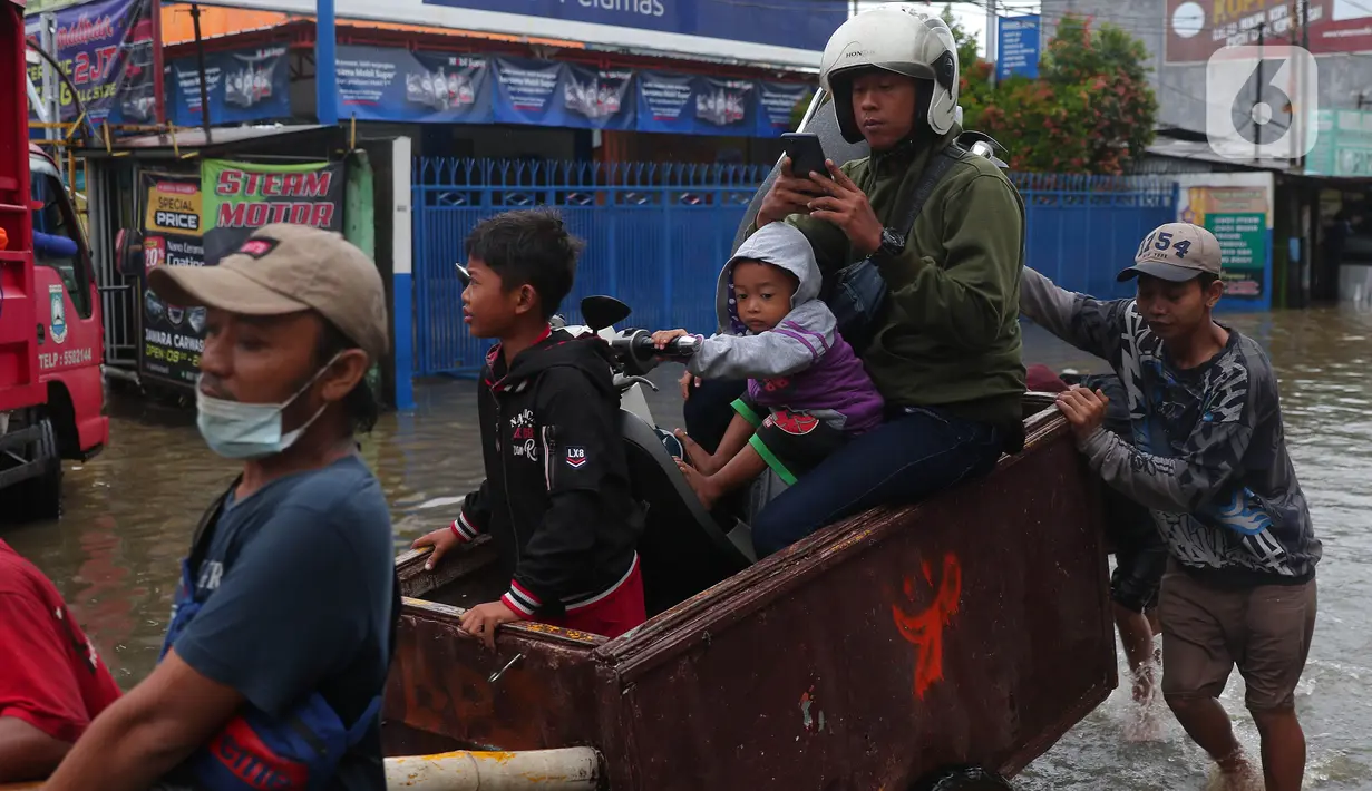 Pengendara bersama sepeda motornya berada di atas gerobak yang didorong pengojek gerobak saat melintasi banjir yang merendam jalan KH Hasyim Ashari, Kota Tangerang, Banten, Sabtu (16/7/2022). Warga sekitar membantu para pengendara yang melintas agar tidak terkena banjir dengan menawarkan jasa gerobak. (Liputan6.com/Angga Yuniar)