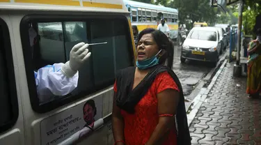 Seorang petugas kesehatan yang mengenakan alat pelindung diri (APD) mengambil sampel swab seorang wanita untuk menguji virus corona Covid-19, dari ambulans di depan pasar kota, di Kolkata (1/9/2020). (AFP/Dibyangshu Sarkar)