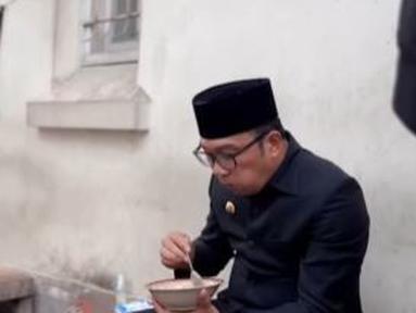 Ridwan Kamil, berjalan kaki bersama asistennya. Di pinggir jalan ia pun berhenti dan menikmati bubur ayam tanpa melepas jas hitam dan peci warna senada. (Foto: Instagram/@ridwankamil)