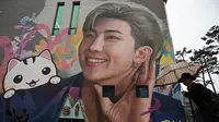 Seorang pria berjalan melewati mural yang menggambarkan RM, salah satu anggota grup K-pop BTS, di Goyang, barat laut Seoul, pada tanggal 11 Desember 2023. (Jung Yeon-je/AFP)