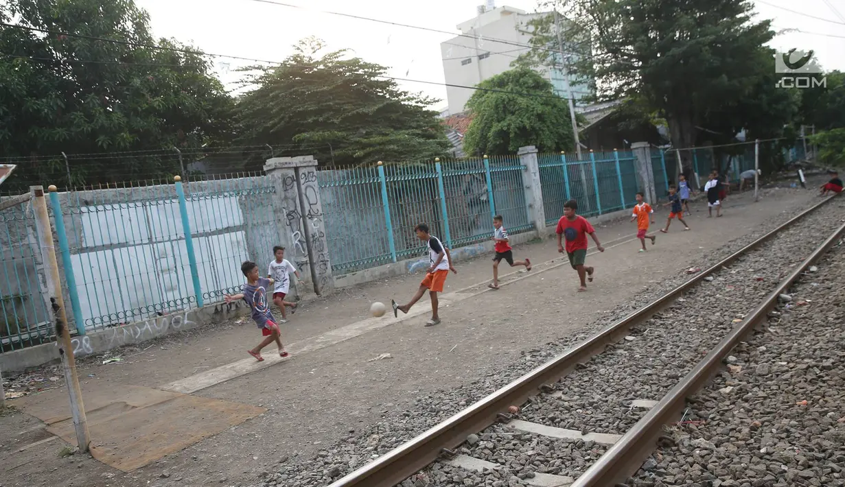 Anak-anak bermain sepak bola di pinggir rel kereta api di kawasan Kemayoran, Jakarta, Senin (24/7). Minimnya lahan bermain menyebabkan anak-anak terpaksa bermain di lokasi tersebut, meskipun berbahaya bagi keselamatan. (Liputan6.com/Immanuel Antonius)