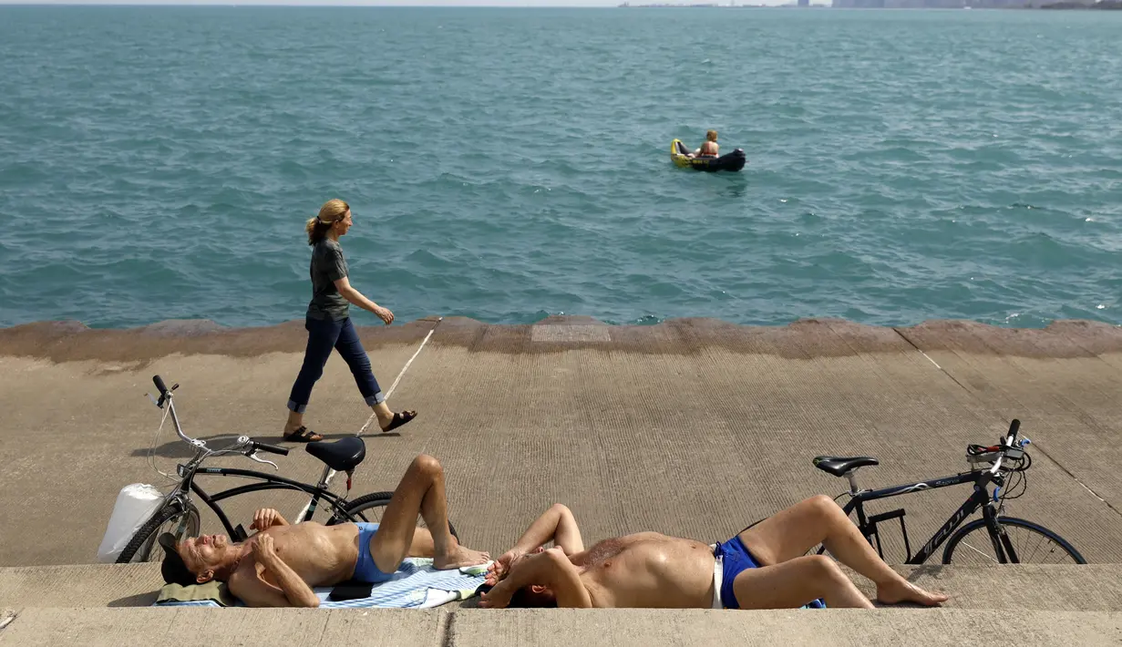Chet Ski (kiri) dan Richard Paul berjemur di Danau Michigan di Montrose Beach, Chicago, Selasa (27/4/2021). Warga AS yang telah menerima vaksin COVID-19 tidak lagi diwajibkan mengenakan masker saat berada di luar ruangan kecuali berada di tengah kerumuman orang asing. (AP Photo/Shafkat Anowar)