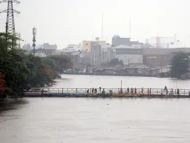 Warga berdiri di salah satu jembatan penghubung Banjir Kanal Barat di Kawasan Tanah Abang, Jakarta, Rabu (1/1/2020). Hujan yang mengguyur Jakarta sejak Selasa sore (31/12/2019) mengakibatkan debit air Banjir Kanal Barat tinggi dan hampir meluap. (Liputan6.com/Helmi Fithriansyah)