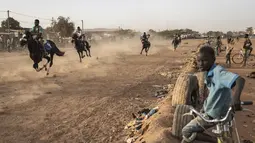 Seorang anak menonton pacuan kuda di Ouagadougou (30/1/2022). Koboi terkenal memenangkan jutaan Franc Afrika Barat dari balapan dan diam-diam melatih kuda di malam hari untuk melakukan dressage, beberapa bahkan menyebut diri mereka koboi dan berpakaian sesuai. (AFP/John Wessels)