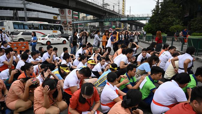 Karyawan pusat perbelanjaan menutupi kepala mereka di sepanjang jalan ketika mereka berpartisipasi dalam latihan gempa di Manila (14/11/2019). Latihan ini sebagai bagian dari kesiapsiagaan nasional menyusul berbagai gempa yang melanda pulau Mindanao bulan lalu. (AFP Photo/Ted Aljibe)