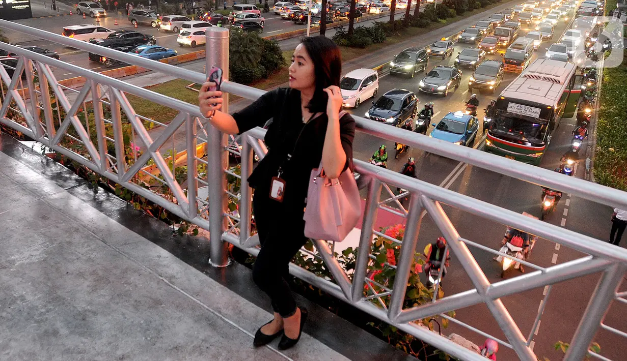 Seorang pejalan kaki berswafoto di jembatan penyeberangan orang (JPO) yang tidak beratap di jalan Sudirman, Jakarta, Rabu (6/11/2019). Pemprov DKI mengklaim mayoritas masyarakat Jakarta setuju dengan konsep JPO terbuka dan tanpa atap yang kini dibangun di Sudirman. (merdeka.com/Arie Basuki)