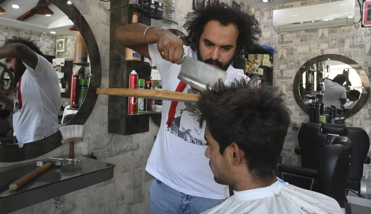 Dalam gambar pada 8 April 2021, tukang cukur Pakistan Ali Abbas menggunakan pisau daging untuk memotong rambut seorang pelanggan di tokonya di Lahore. Berharap membuktikan kemampuannya dalam persaingan, Ali Abbas mengandalkan berbagai alat yang tidak biasa untuk melatih keahliannya. (Arif ALI/AFP)