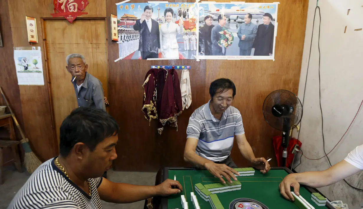 Para nelayan saat bermain mahjong di depan poster Presiden China Xi Jinping saat perahunya bersandar akibat badai Topan Chan-Hom yang mendekati wilayah Wenling, Zhejiang, China (8/7/2015). (REUTERS/William Hong)
