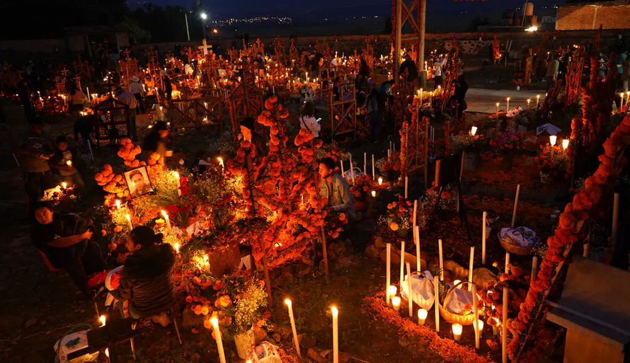Kerabat menghabiskan malam di samping makam orang yang mereka cintai pada perayaan Hari Kematian di pemakaman Arocutin, Michoacan, Meksiko, 1 November 2021. Tradisi ini bertepatan dengan Hari Semua Orang Kudus dan Hari Semua Jiwa. (AP Photo/Eduardo Verdugo)