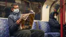 Seorang pria memakai masker saat membaca koran di kereta bawah tanah London, di London, Kamis (16/12/2021). Inggris mencatat jumlah tertinggi infeksi COVID-19 baru yang dikonfirmasi pada hari Rabu (15/12) sejak pandemi dimulai. (AP Photo/Alberto Pezzali)