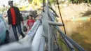 Warga berjalan di samping pagar jembatan yang rusak di kawasan Bukit Duri, Jakarta, Jumat (21/2/2020). Pagar yang rusak akibat penanganan sampah banjir tersebut hingga kini belum juga diperbaiki. (Liputan6.com/Immanuel Antonius)