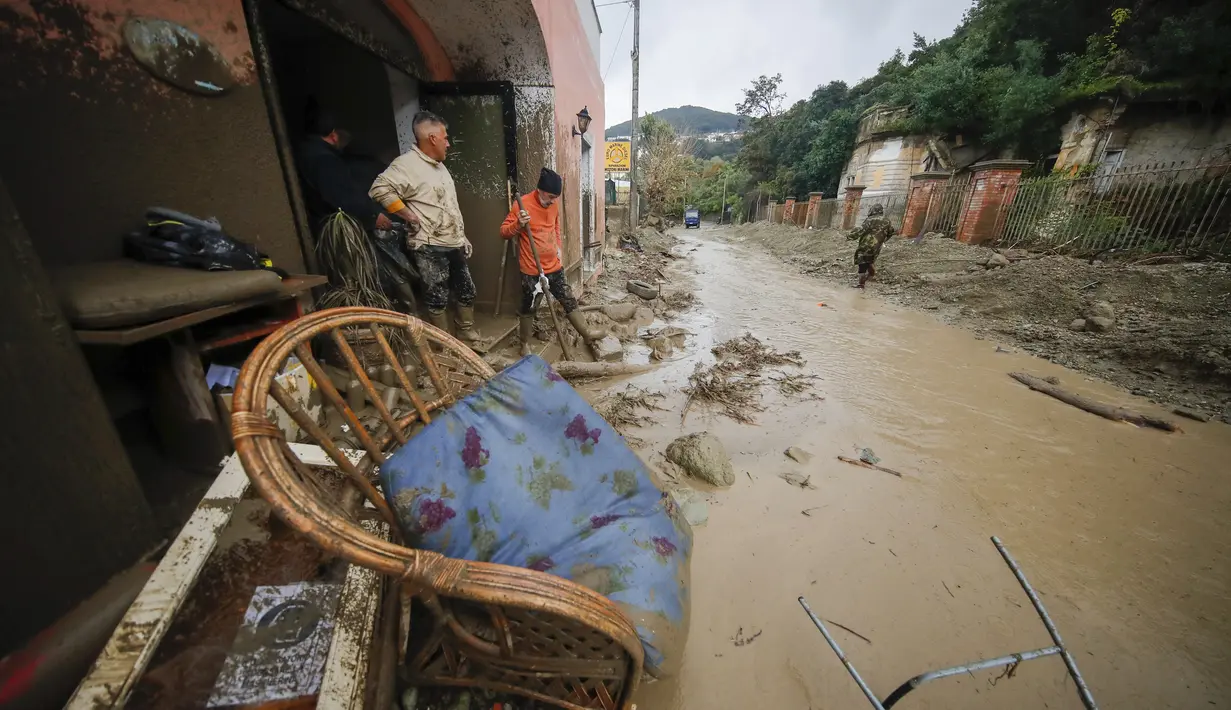 Orang-orang berdiri di depan toko yang terendam banjir setelah hujan lebat memicu tanah longsor yang meruntuhkan bangunan dan menyebabkan 12 orang hilang, di Casamicciola, di pulau Ischia, Italia selatan, Sabtu, 26 November 2022. Petugas pemadam kebakaran sedang melakukan upaya penyelamatan karena bala bantuan sedang dikirim dari Napoli terdekat, tetapi mengalami kesulitan dalam mencapai pulau baik dengan perahu motor atau helikopter karena cuaca. (AP Photo/Salvatore Laporta)