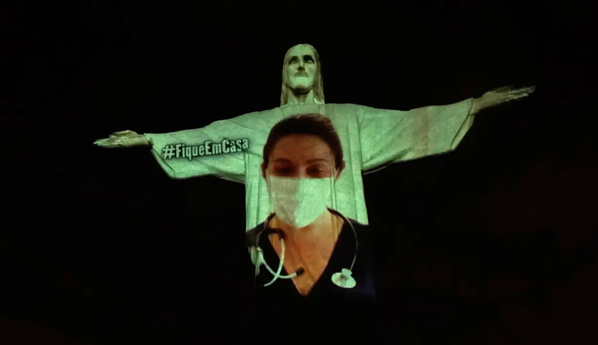 Patung Christ the Redeemer yang populer di dunia menyala dengan gambar seorang dokter selama kebaktian Paskah di Rio de Janeiro, Brasil, Minggu (12/4/2020). Pertunjukkan itu bentuk solidaritas kepada dokter dan perawat yang telah merawat pasien corona di berbagai negara. (AP/Silvia Izquierdo)