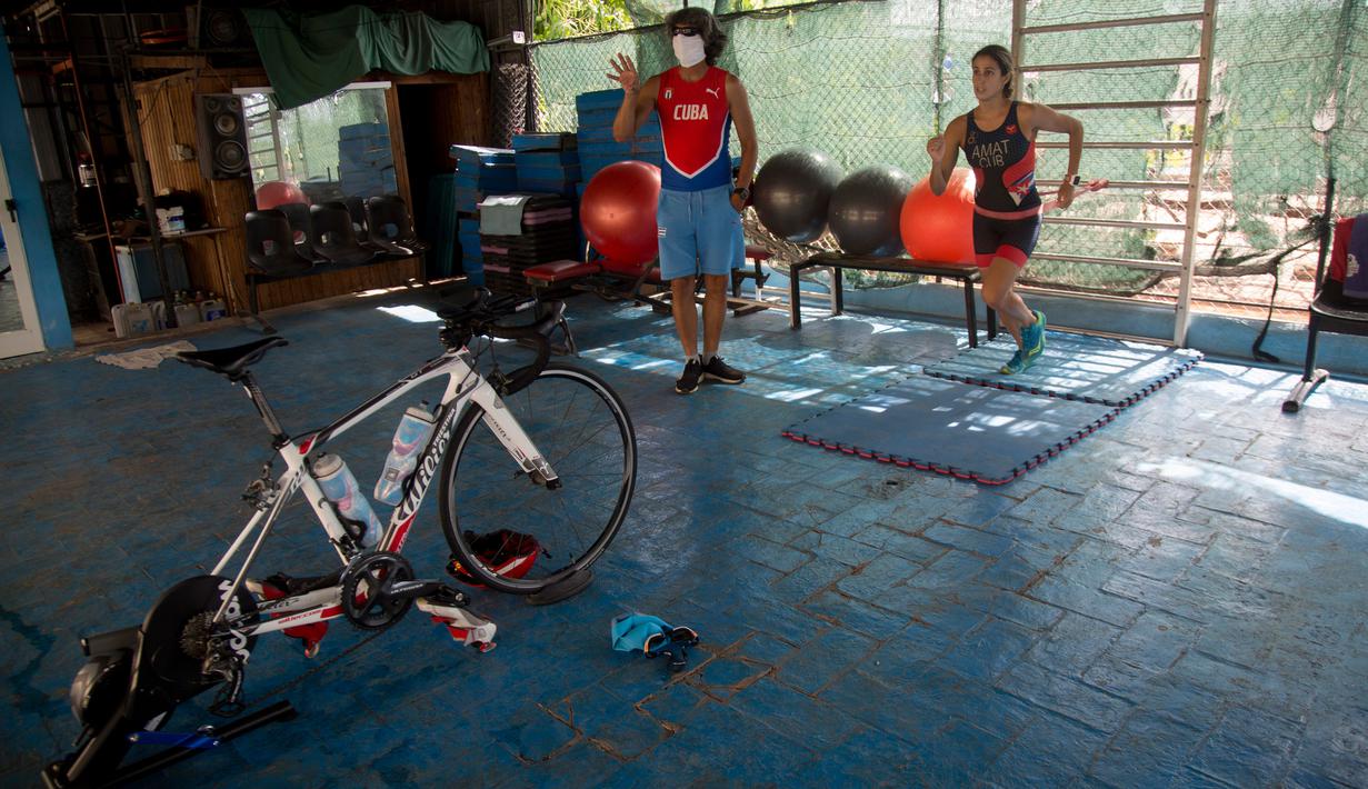 Atlet triathlon Kuba, Leslie Amat berlari dengan tali di pinggangnya di bawah pengawasan sang pelatih, Dioseles Fernandez di teras rumahnya di Havana, Senin (20/4/2020). Atlet Kuba tak bisa berlatih di fasilitas olahraga seperti biasanya selama pademi corona. (AP /Ismael Francisco)