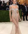 Kendall Jenner tampil bergaya ‘naked’ dalam balutan sheer gown bertabur kristal berkilau rancangan Givenchy. Penampilannya yang glamor tersebut diperlengkap dengan kalung choker besar. Model 25 tahun ini menjaga rambutnya tetap sederhana dengan sanggul rendah. (Instagram/_metgala2021).